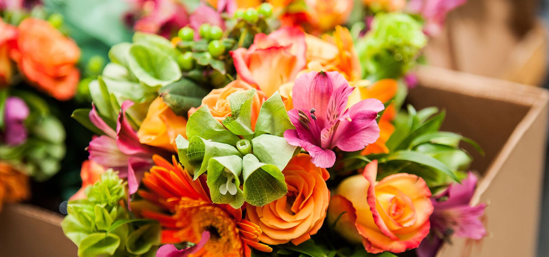 Nahaufnahme eines farbenfrohen Blumenstraußes in Orange- und Pinktönen mit Rosen und Gerbera in einem Karton.